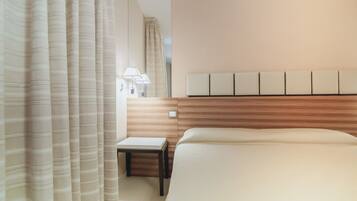 A modern hotel room with a large bed, a bedside table, a lamp, and a headboard with a light panel.