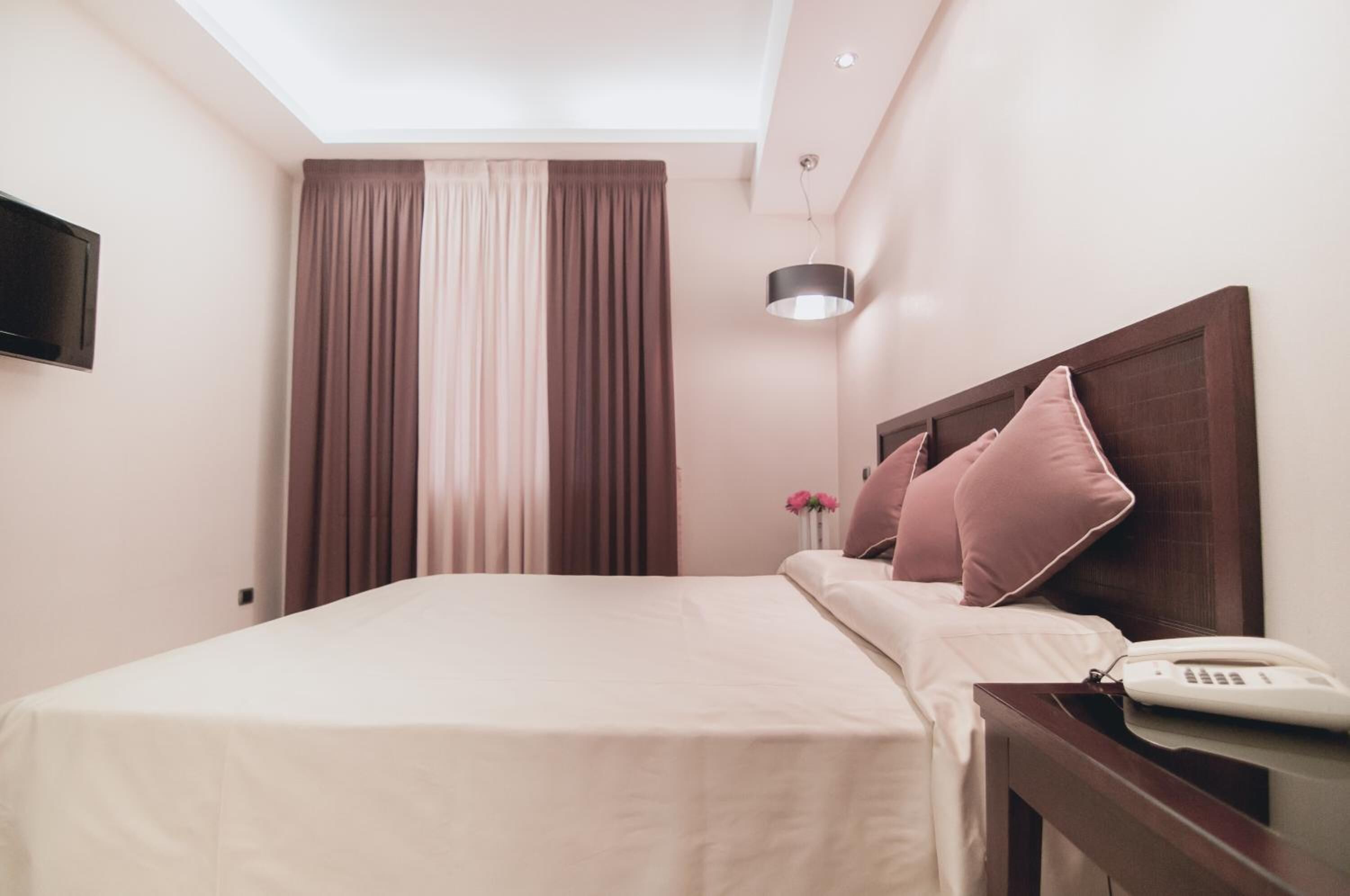 Une chambre d’hôtel avec un lit, une table de chevet avec un téléphone, une lampe et un téléviseur fixé au mur.