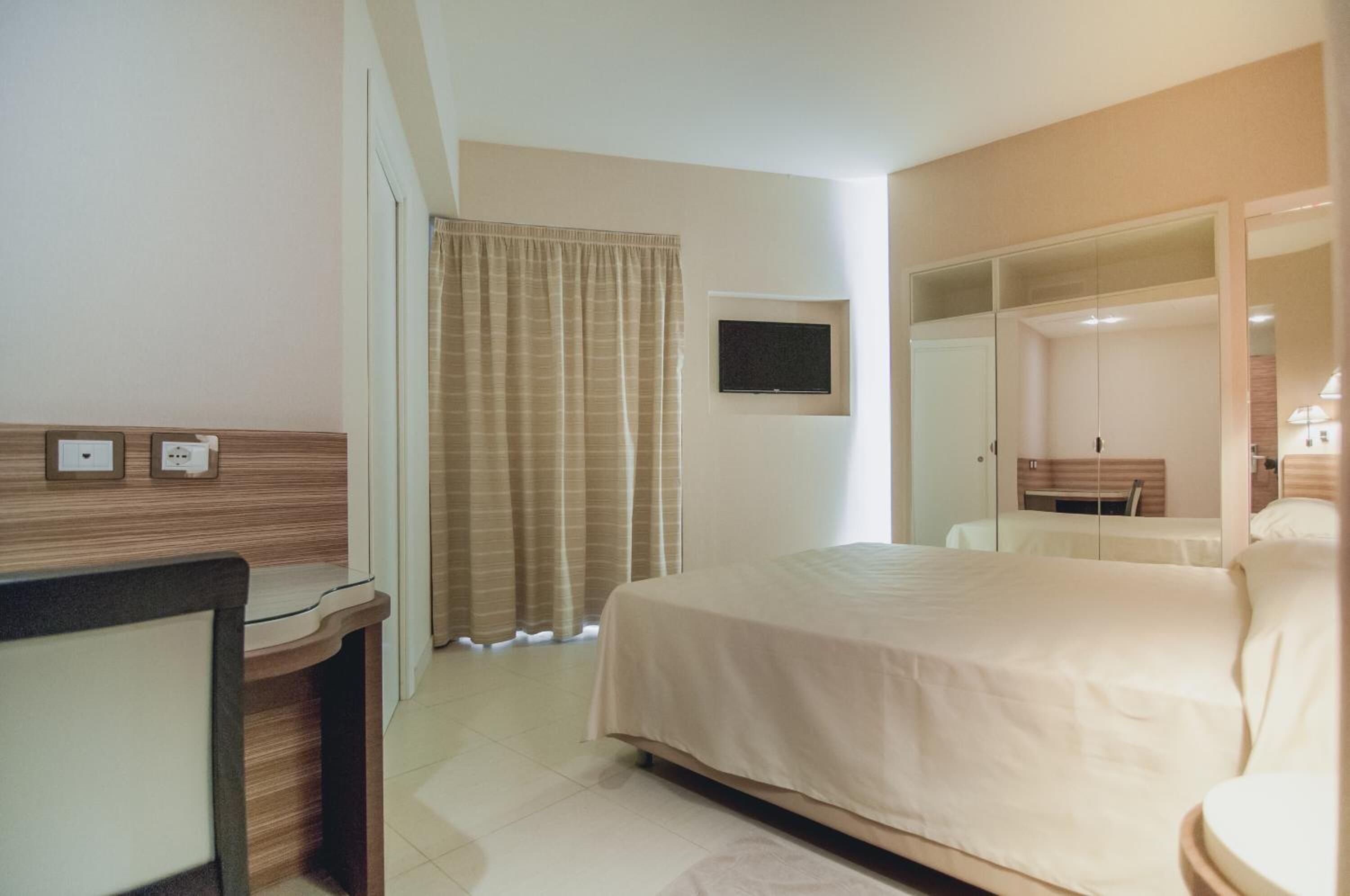 A hotel room with a bed, a desk, a television, and a mirror.