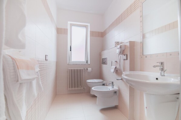 A bathroom with a toilet, bidet, and sink, a window, and a towel rack.