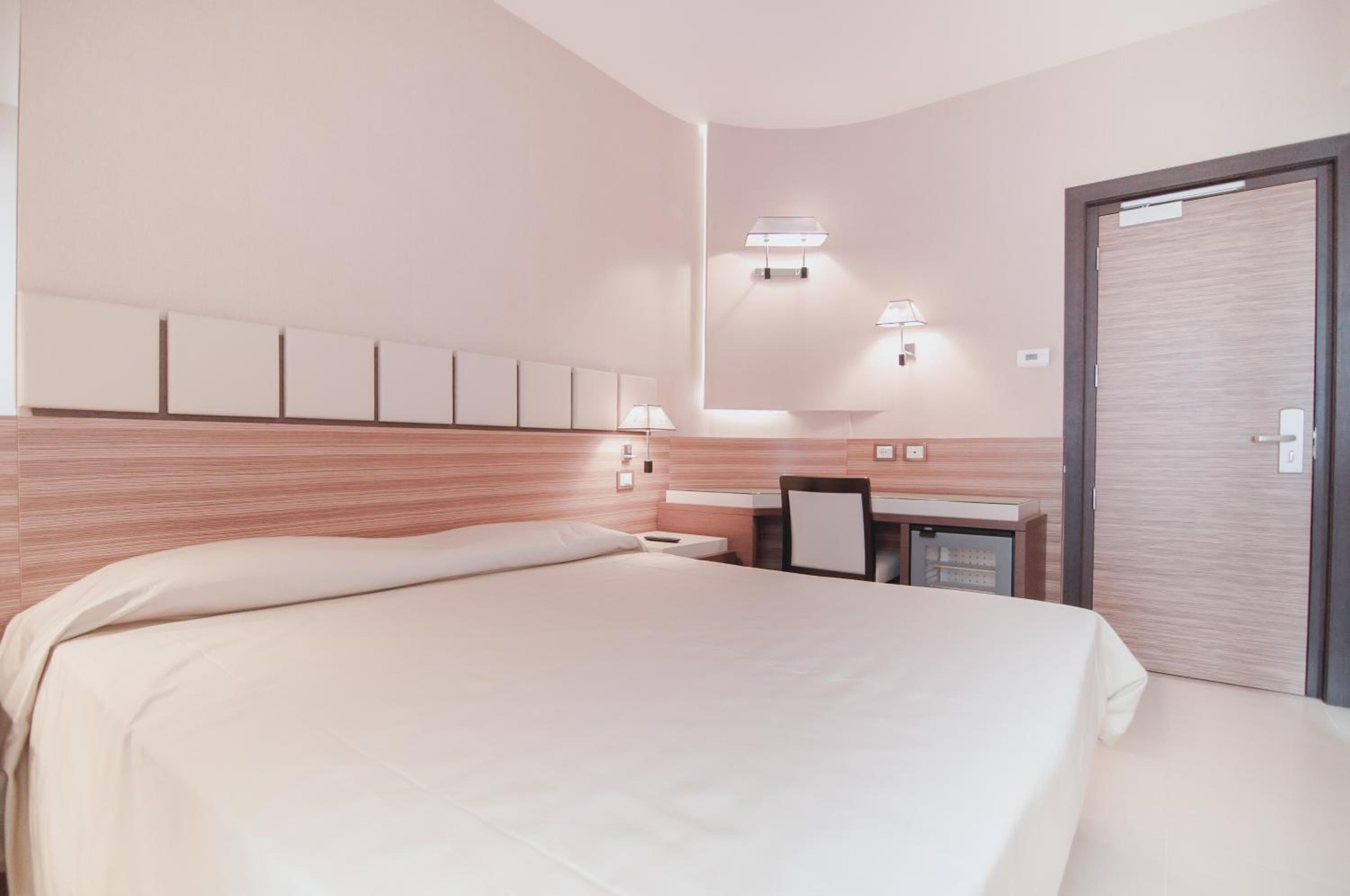 A hotel room with a large bed, a desk, and a wardrobe.