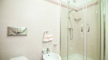 Un baño con ducha envuelta en vidrio, un lavamanos y un inodoro.