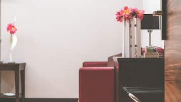 A hotel room with a red armchair, a small table with a vase of flowers, and a lamp.