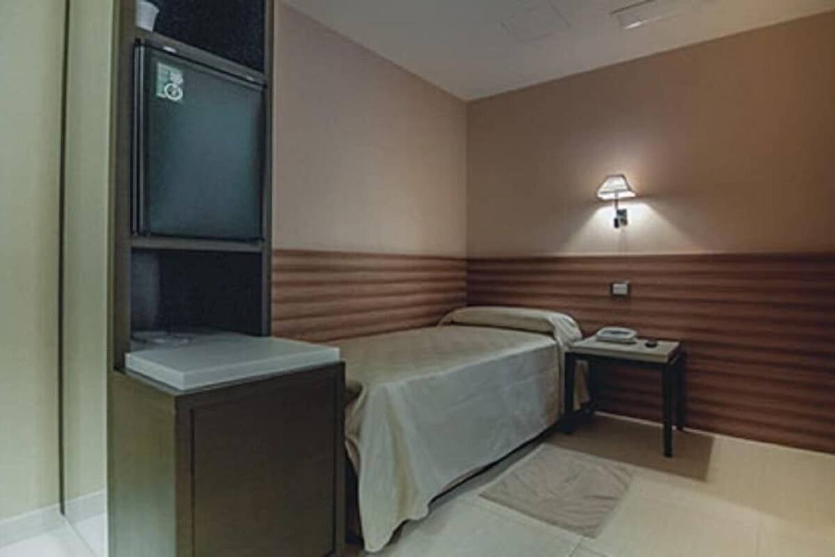 Une petite chambre à coucher, bien rangée, avec un lit, une table de chevet et une lampe fixée au mur.
