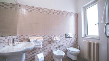 Een badkamer met een wastafel, bidet, toilet en een raam, met een handdoek aan de radiator.