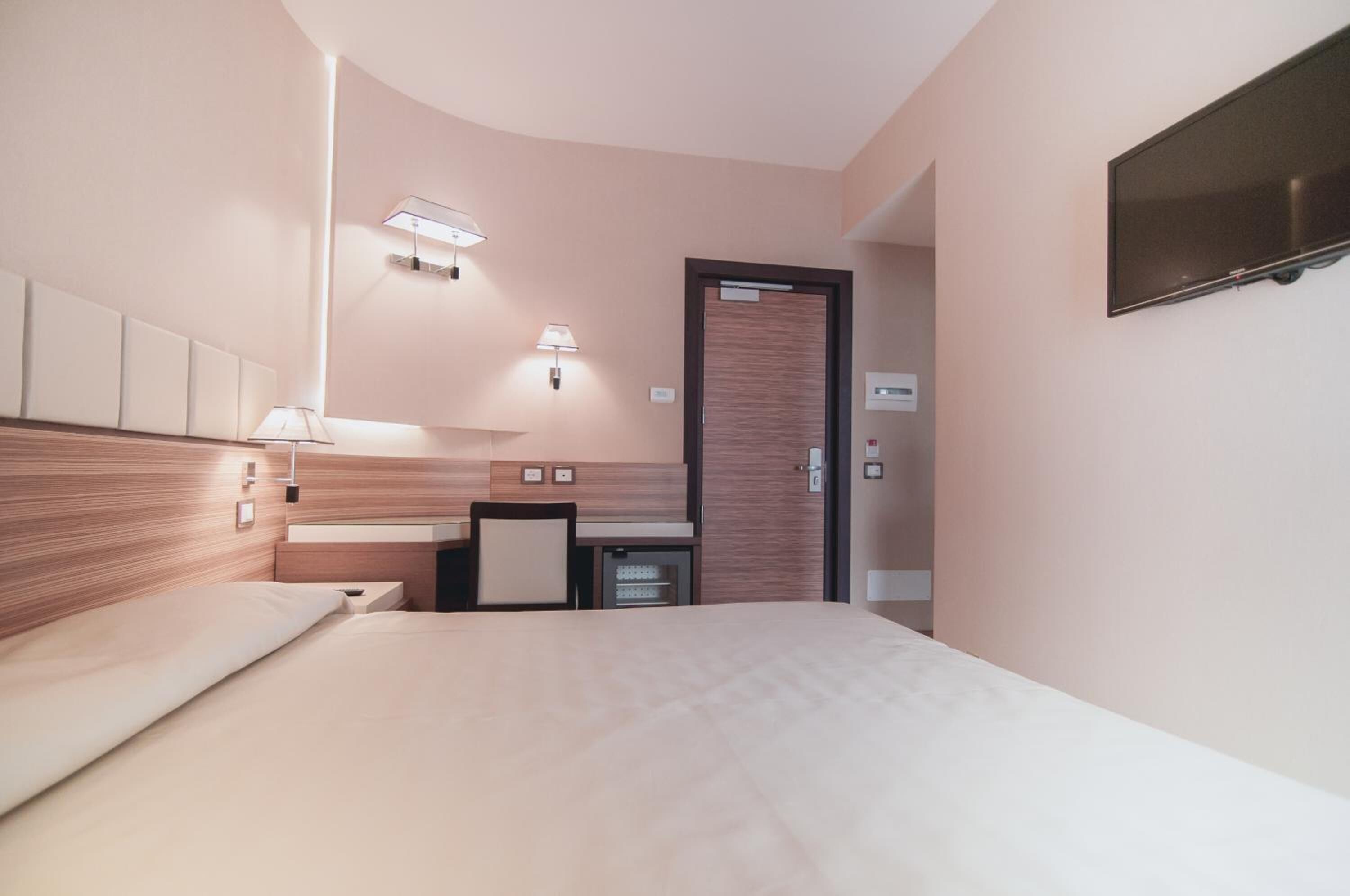 A modern hotel room with a bed, bedside tables, a desk, and a TV mounted on the wall.