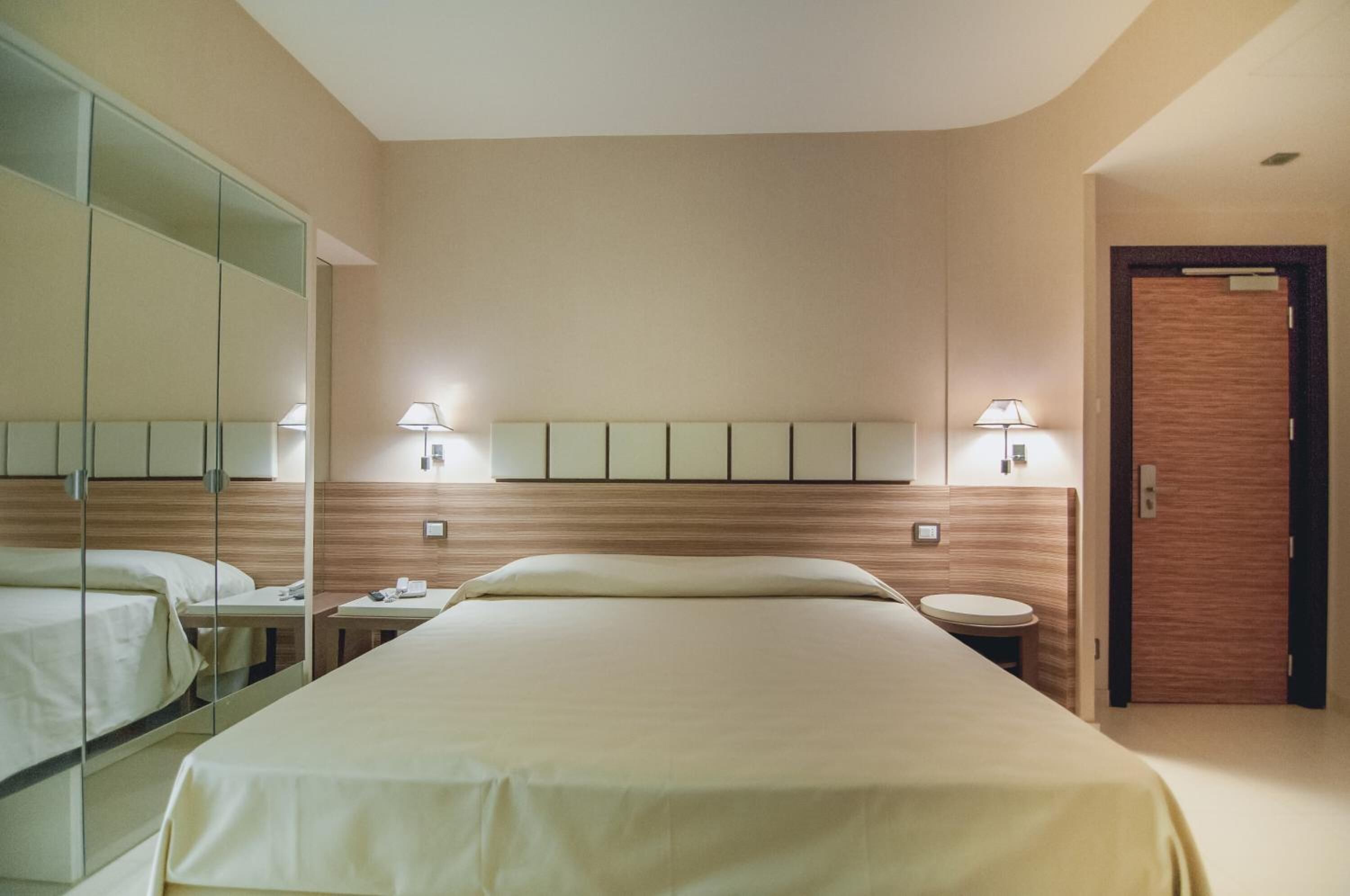 A hotel room with a large bed, bedside tables, a mirror, and a wooden door.
