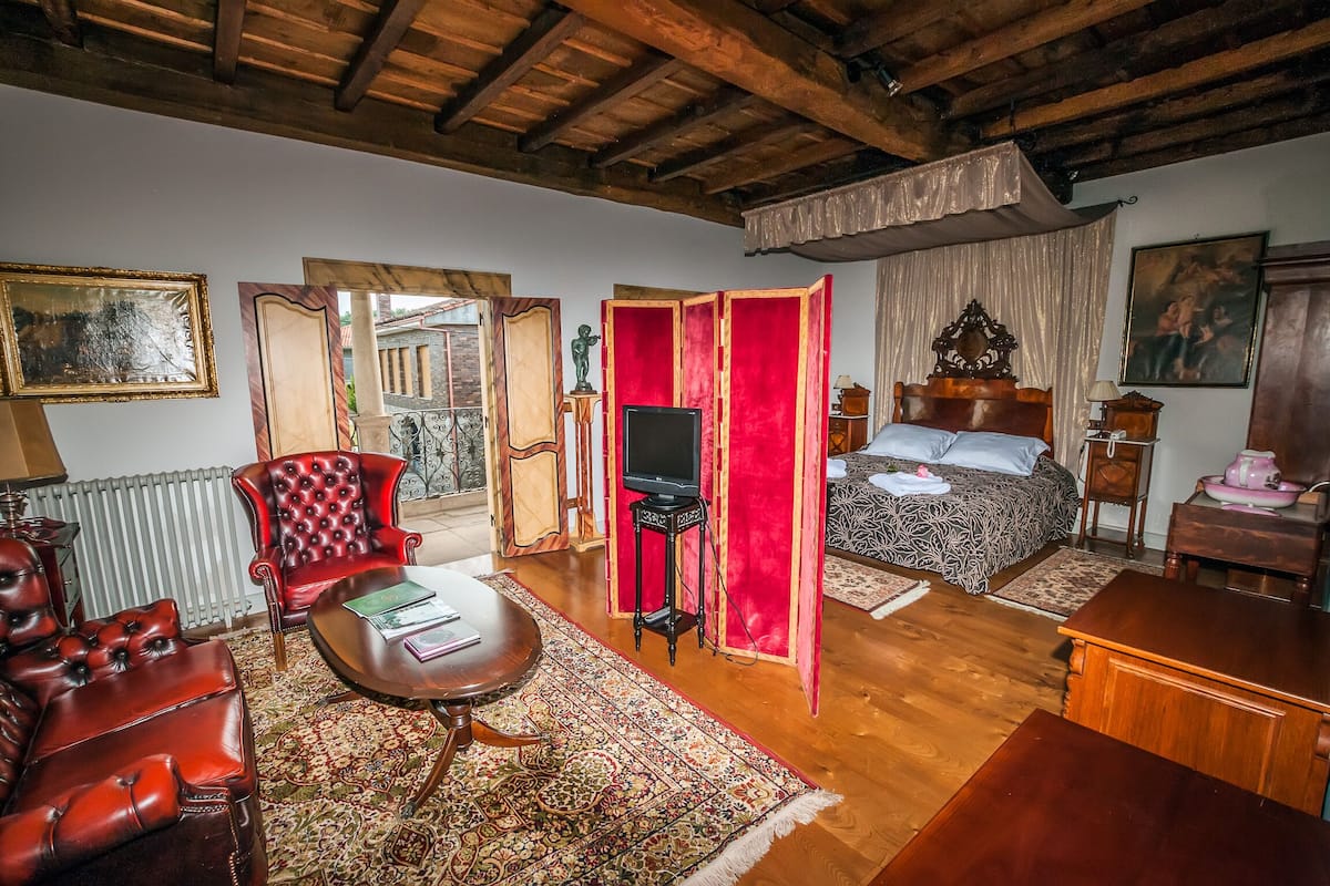 Ein Zimmer mit einem Bett, einem Fernseher, einer roten Trennwand, einem roten Sessel, einem Tisch und einer Heizung.