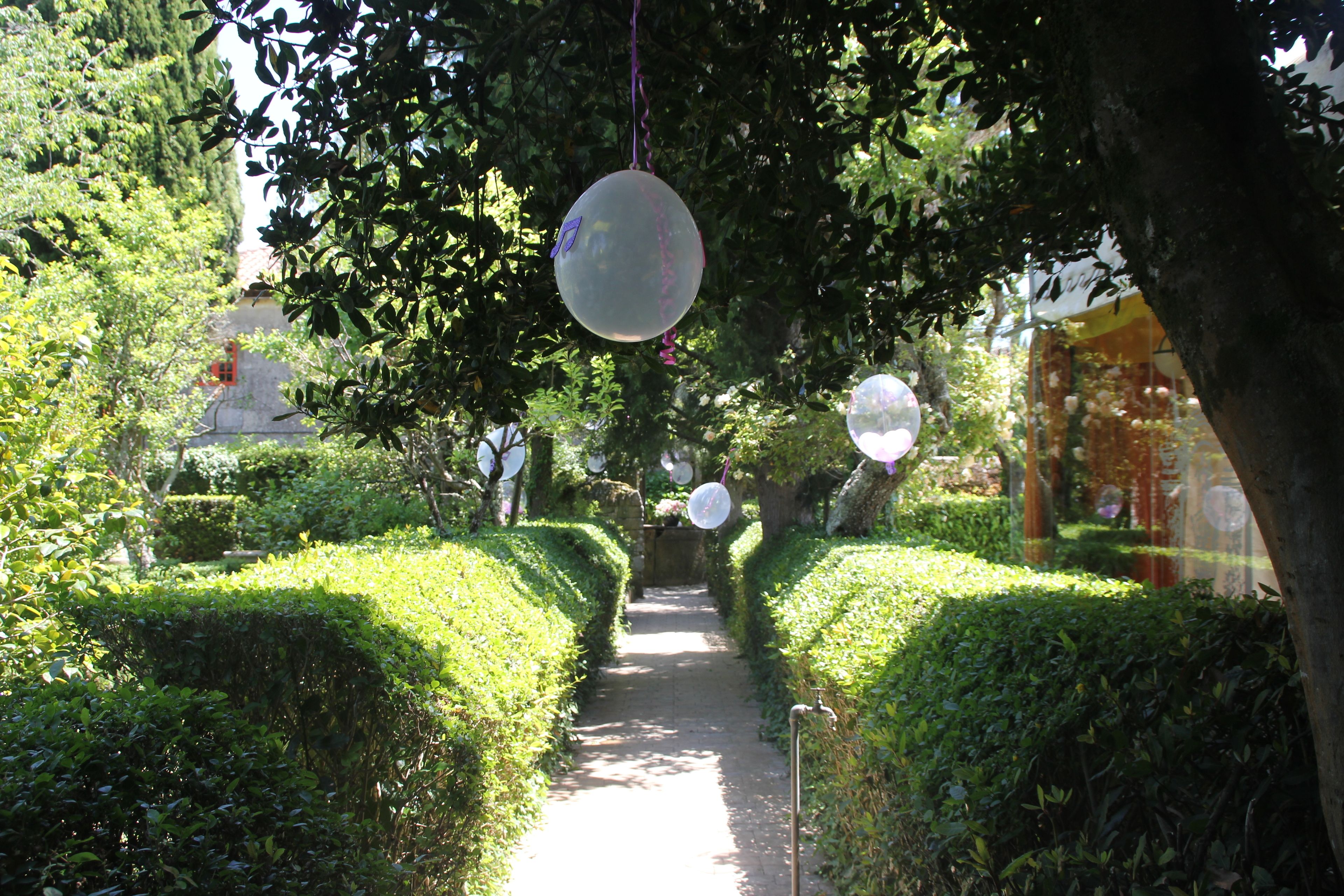 Un sentier bordé de haies et d’arbres soigneusement taillés, avec des objets sphériques suspendus aux branches.