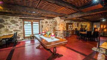 Un coin repas rustique avec un mur en pierre, un plafond en bois et une table centrale décorée de bougies et de fruits.