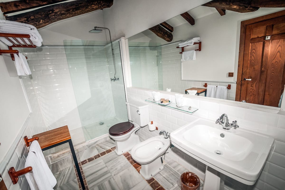 Ein Badezimmer mit Duschkabine, Toilette, Bidet, Waschbecken und einem spiegel mit Holzrahmen.