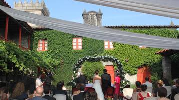 An outdoor wedding ceremony with guests seated on white chairs, a bride in a white dress, and a groom in a suit.