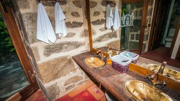 Un baño con dos lavamanos, un espejo y toallas colgadas en una pared de piedra.