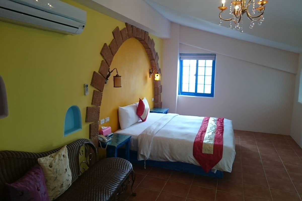 A bedroom with a bed, a sofa, a chandelier, and a window.