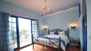 A bedroom with a bed, a chandelier, a balcony with chairs, and a view of the outdoors. - Greece Style Hotel (Hengchun)