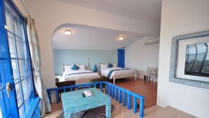 A bedroom with two beds, a blue table, and a window with a view. - Greece Style Hotel (Hengchun)