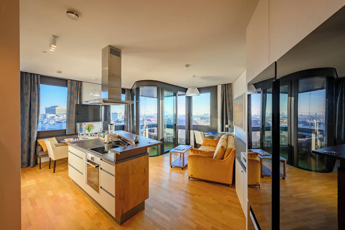 A modern apartment with a kitchen, dining area, and living room, featuring large windows and a city view.