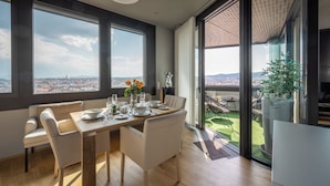 A dining area with a table set for four, large windows, and a view of the cityscape. - Skyflats Vienna - Rooftop Apartments (Vienna)