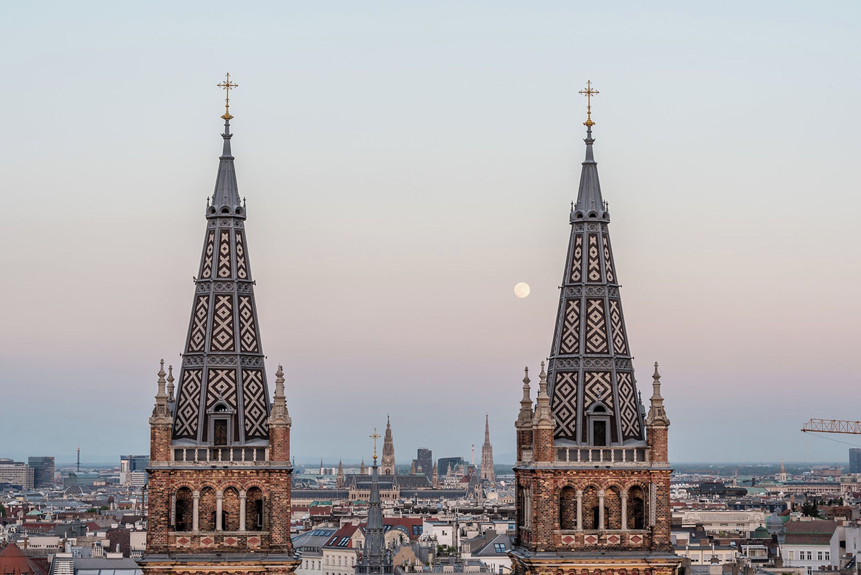 Two prominent towers with intricate patterns, a cityscape in the background, and a visible moon.