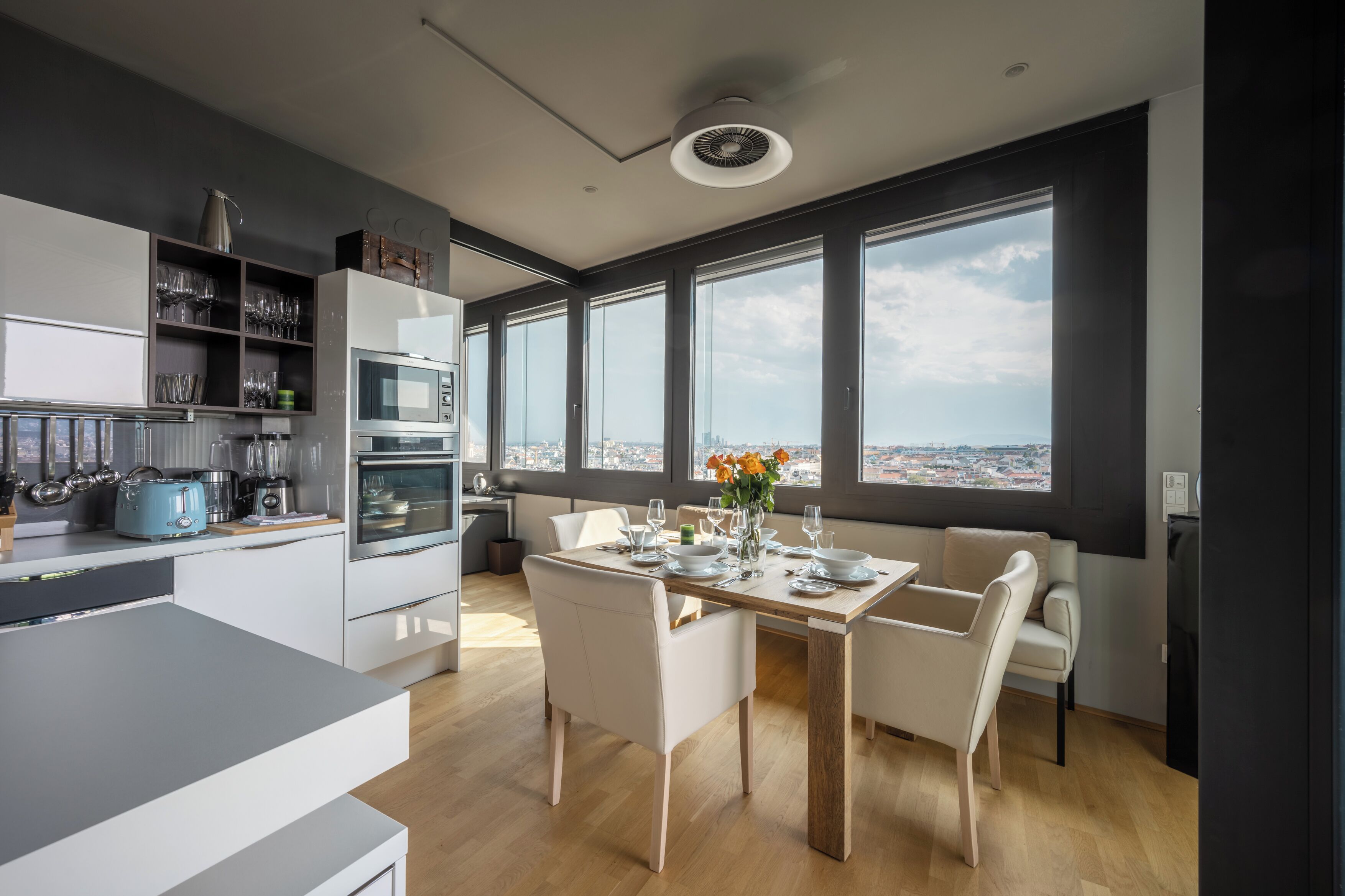 A modern kitchen with a dining area, large windows, and a view of the city.