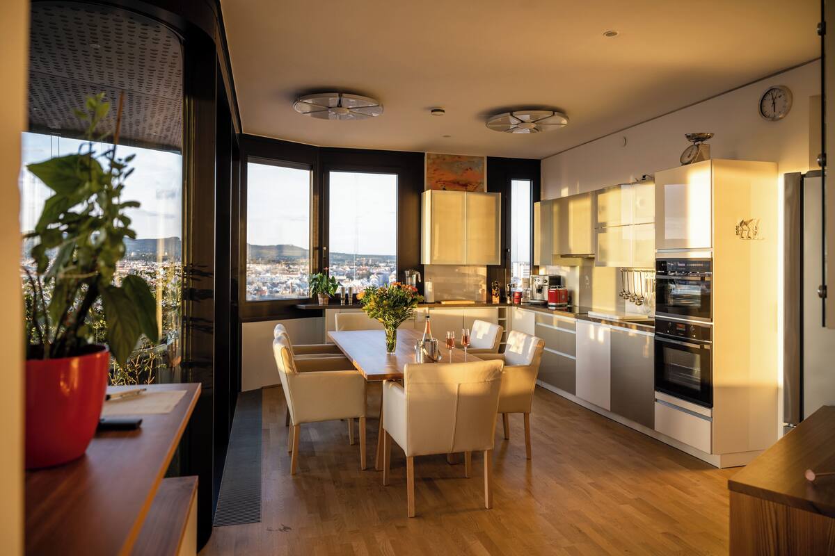 A modern kitchen with a dining area, large windows, and a view of the city.