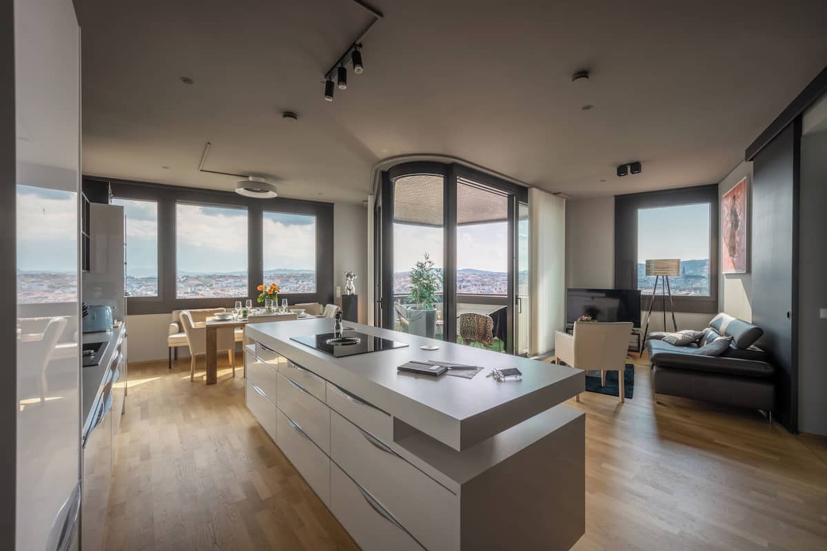 A modern kitchen with a central island, large windows offering a city view, and a dining area with a view.