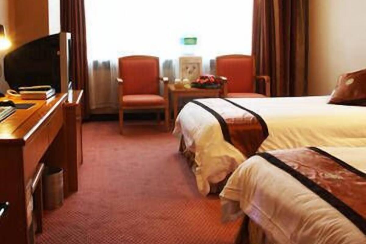 A hotel room with a bed, a desk with a computer, a chair, and a small table with a lamp.