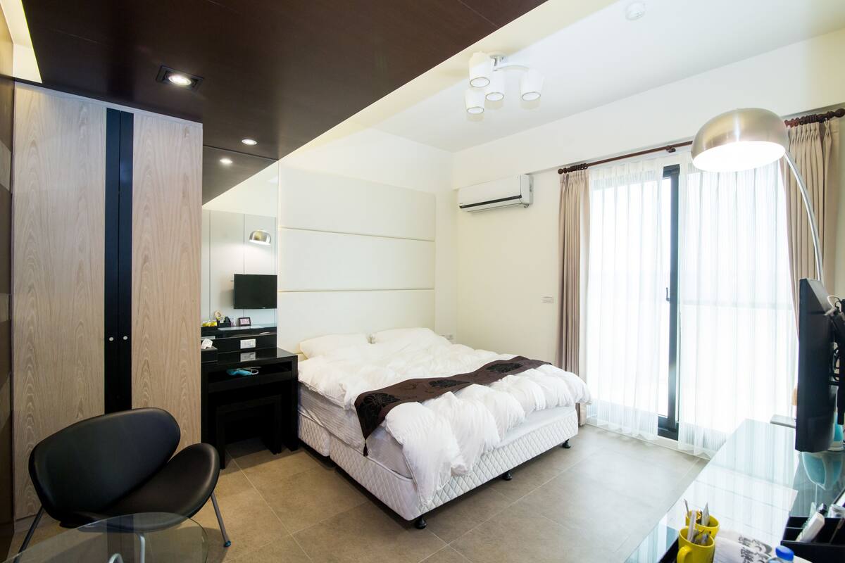 A modern hotel room with a bed, a desk, a chair, and a TV.