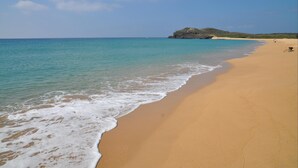 A wide sandy beach with gentle waves, a clear sky, and a distant rocky outcrop. - Ai Lian Shan Shui Homestay (Magong)