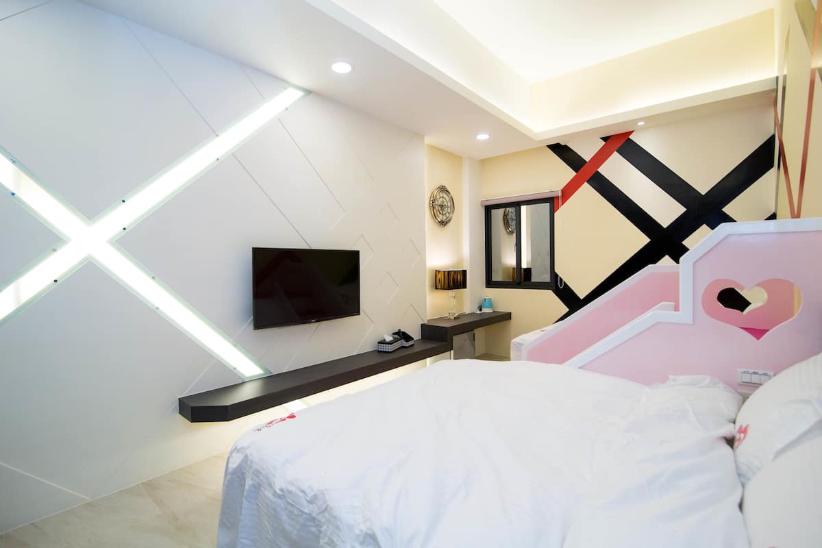 A modern bedroom with a bed, a TV mounted on the wall, and a desk with a lamp.