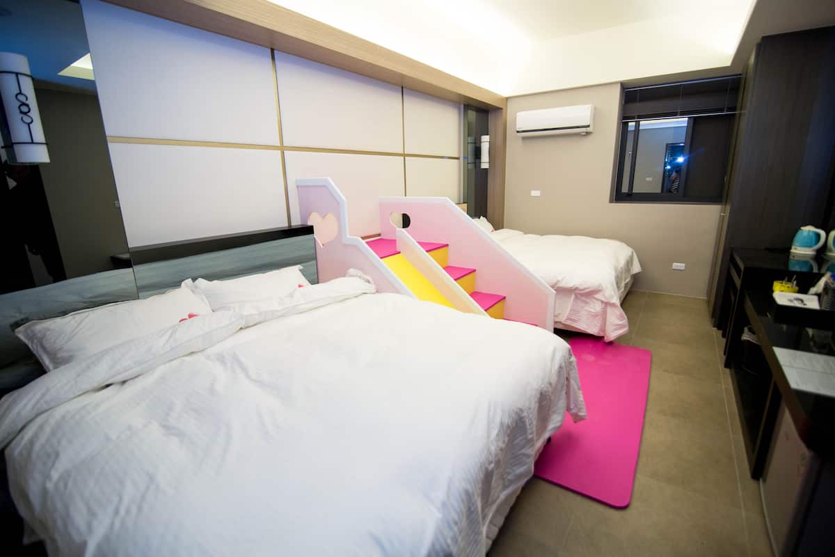 A hotel room with two beds, a pink exercise mat, a mirror, and a small desk with a chair.