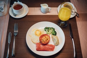 A breakfast plate with eggs, broccoli, tomato, and ham on a table with cutlery and a cup of tea.