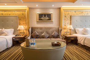 A hotel room with two beds, a sofa, a glass coffee table, and a framed artwork on the wall.