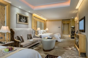 A hotel room with a sofa, two beds, a round coffee table, and a TV.