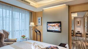 A hotel room with a large bed, a TV mounted on the wall, a desk with a lamp, and a view of the city through large windows. - Sunshine Hotel Zhangjiajie (Zhangjiajie)