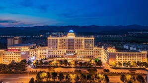 A large, multi-story hotel with a prominent dome and illuminated signage, surrounded by a well-maintained landscape and a view of distant mountains. - Sunshine Hotel Zhangjiajie (Zhangjiajie)
