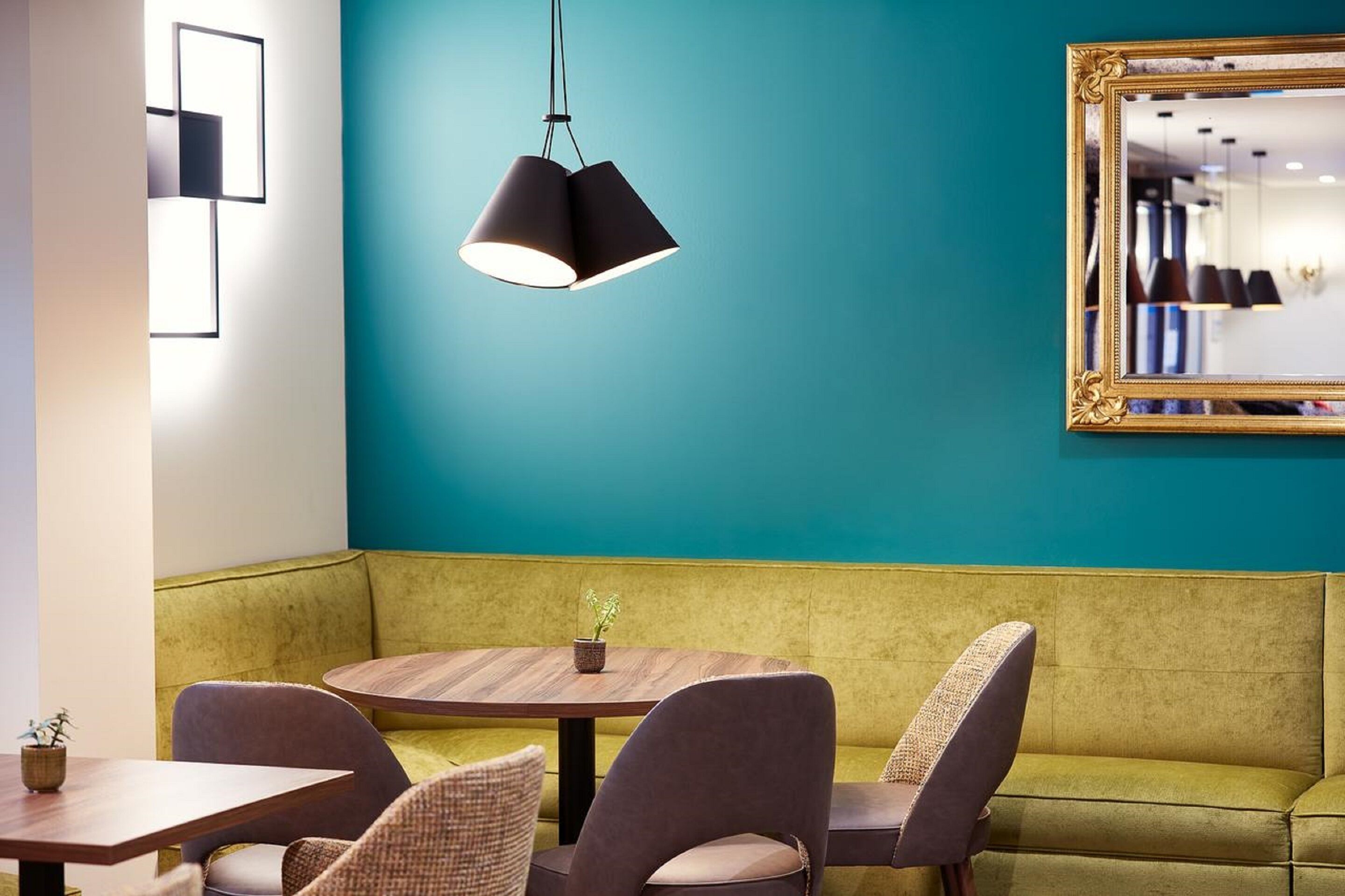 A modern interior with a teal accent wall, a round wooden table, and a green sofa.