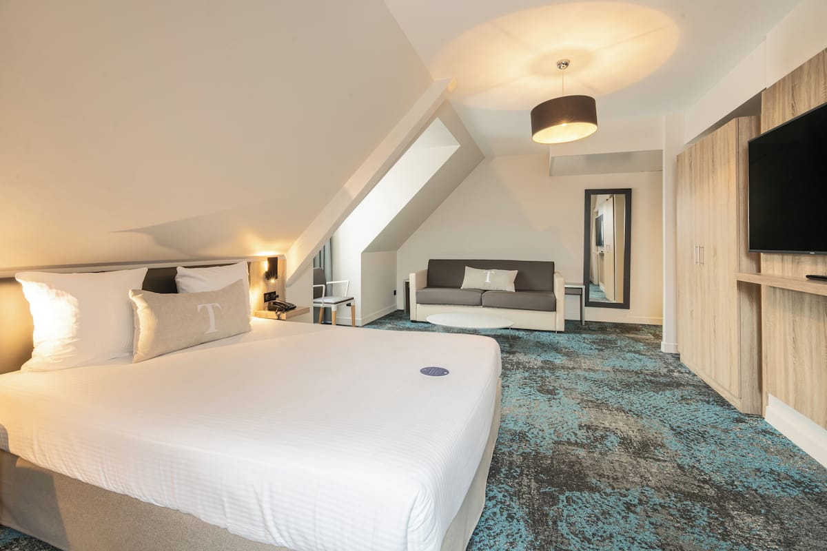 A modern hotel room with a large bed, a TV, a sofa, and a mirror.