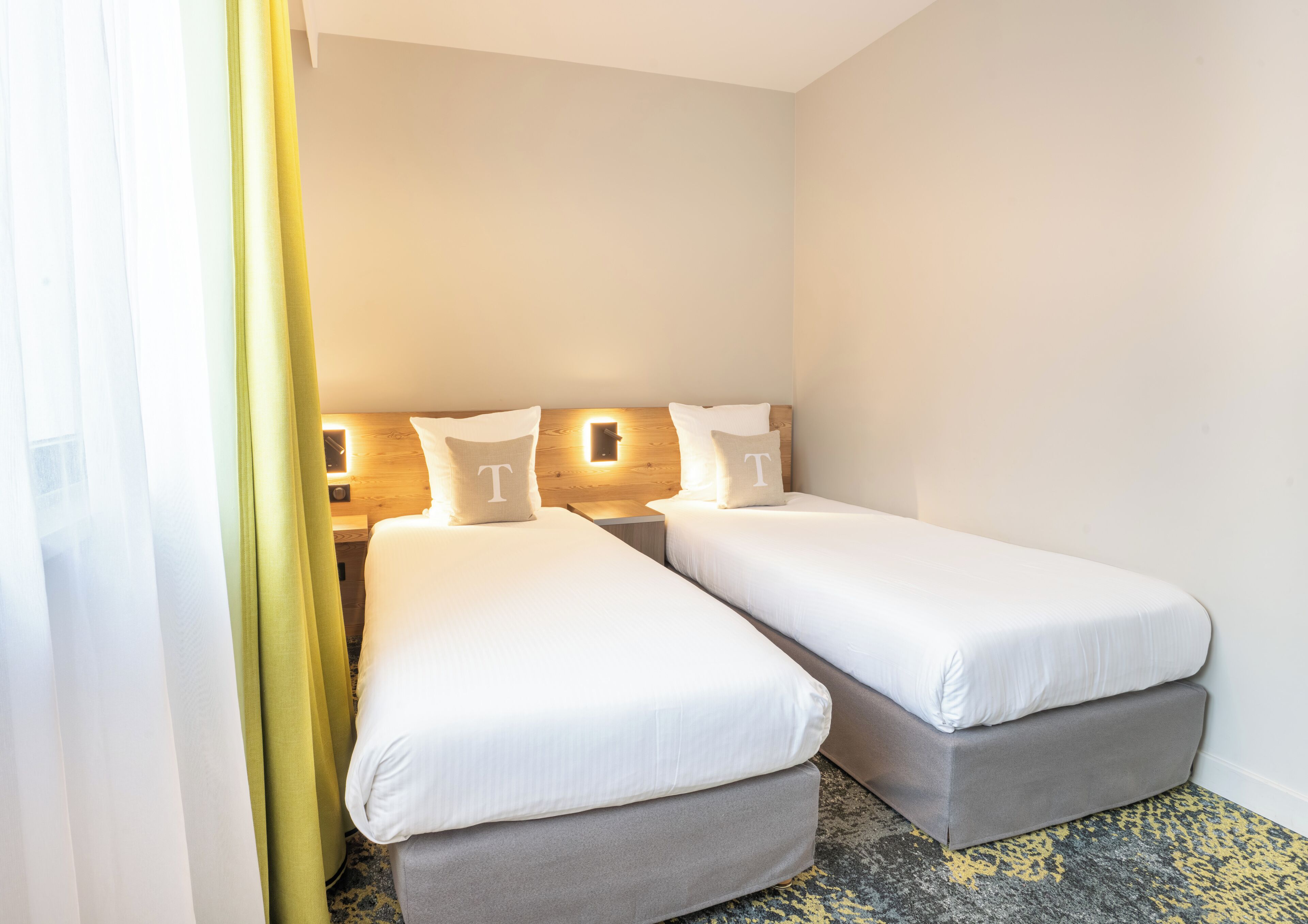 Hotellihuone, jossa on kaksi erillistä sänkyä, puinen pääty, yöpöytävalaisimet ja kuviollinen matto.