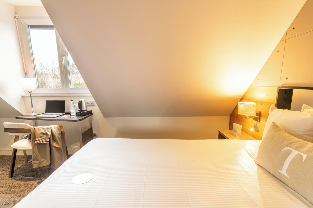 A hotel room with a bed, desk, chair, lamp, and a window.