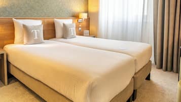 Ein Hotelzimmer mit zwei Betten, einer Wand mit Muster, einem Fenster mit Vorhängen und einem Nachttisch mit Lampe.