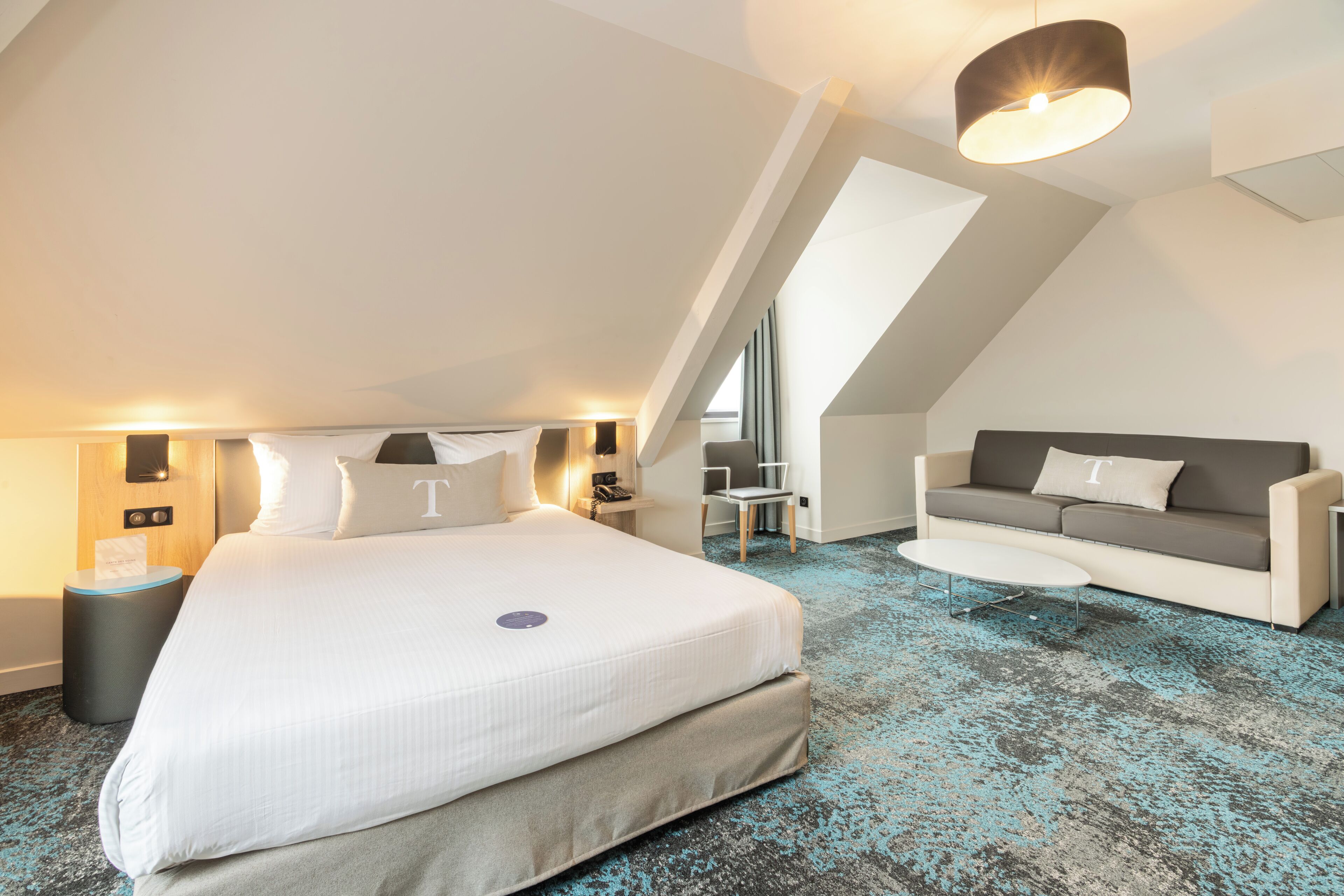 Une chambre d’hôtel moderne avec un grand lit, un canapé, une petite table et un luminaire au plafond.