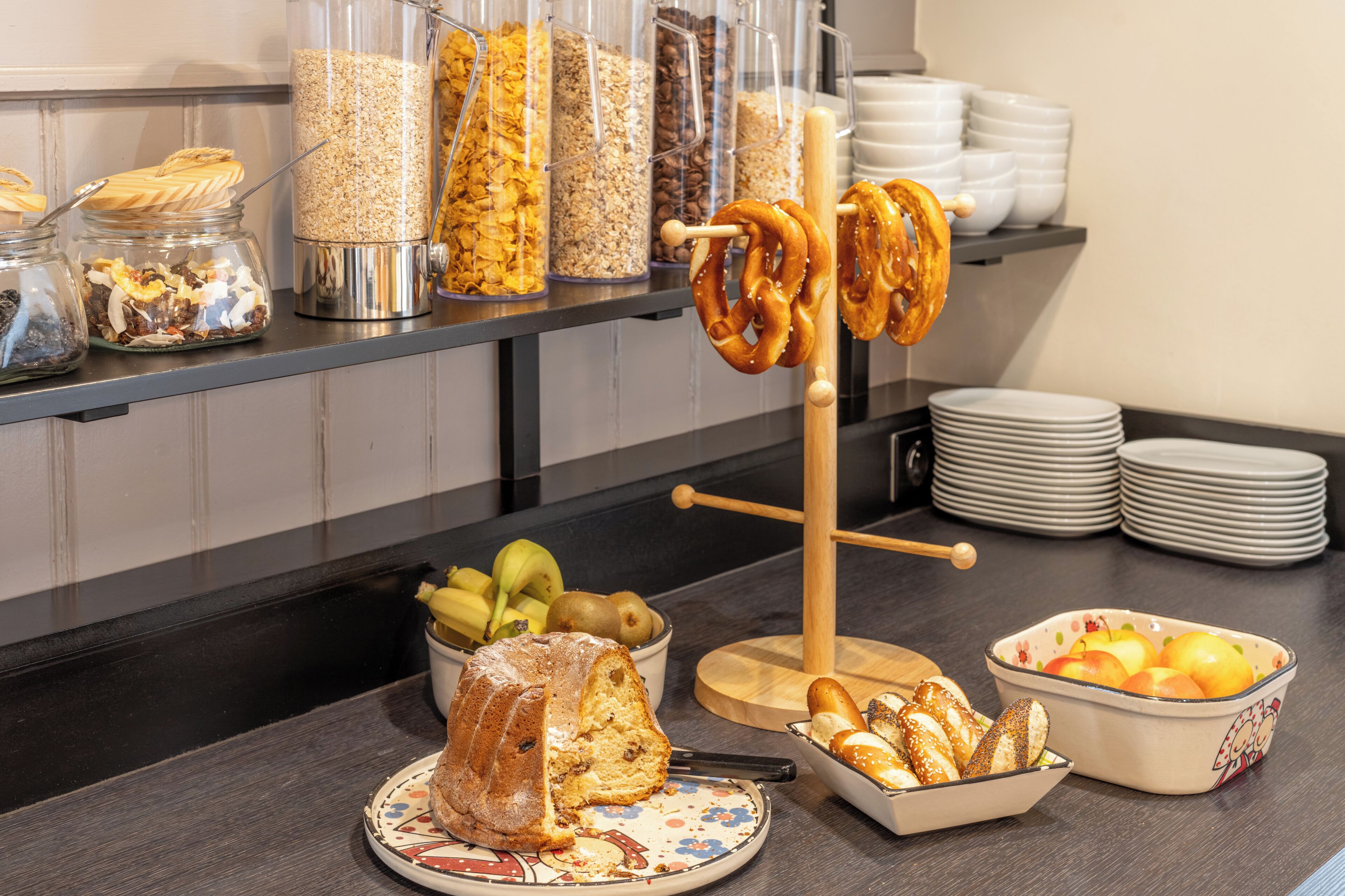 Un bufé con diversos alimentos, como un pastel bundt, pretzels y tazones de frutas y frutos secos.