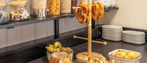 Un bufé con diversos alimentos, como un pastel bundt, pretzels y tazones de frutas y frutos secos.