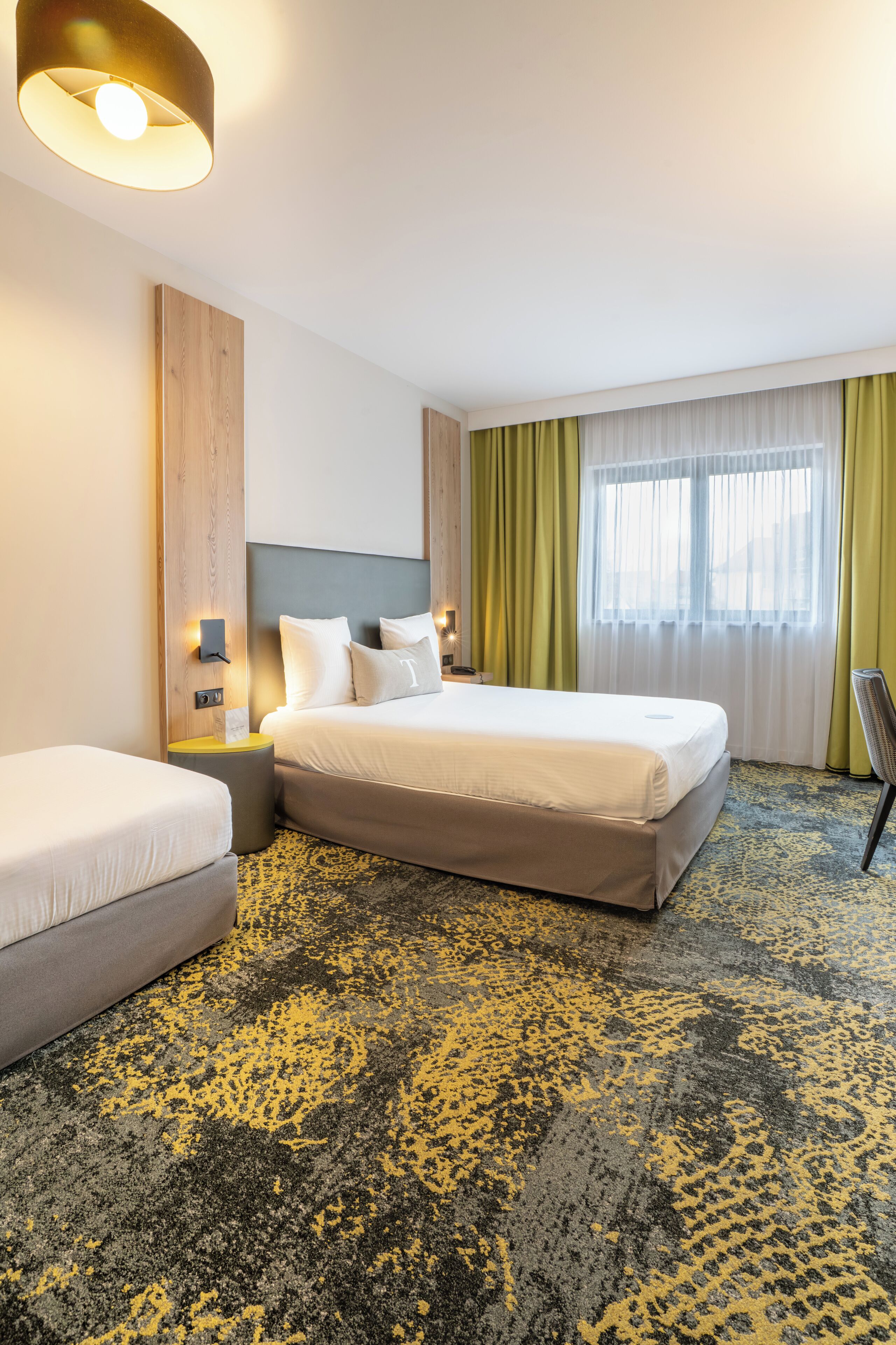 Una habitación de hotel con cama, mesita de noche, silla y ventana con cortinas.