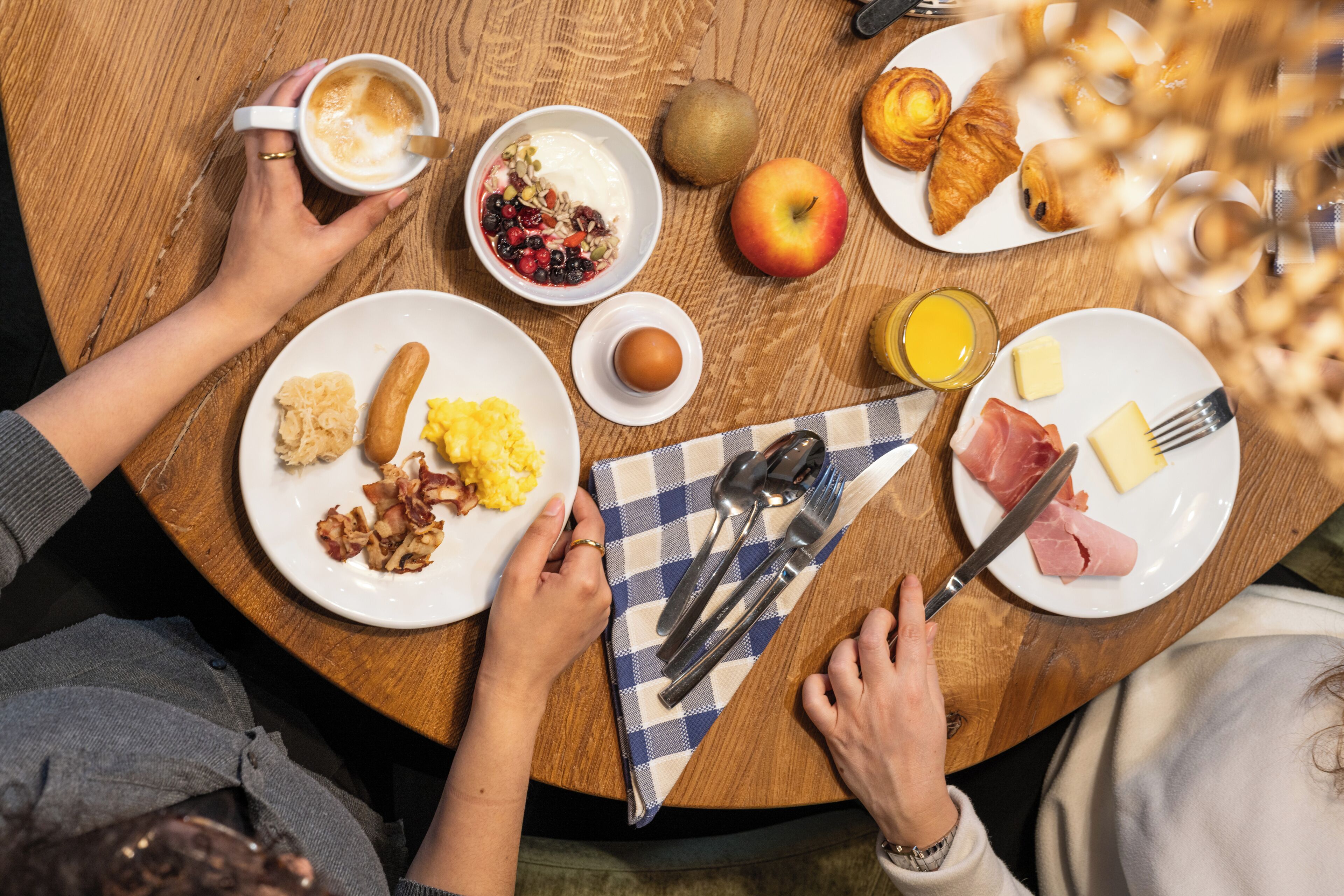 A round wooden table with breakfast items including croissants, eggs, and fruits.