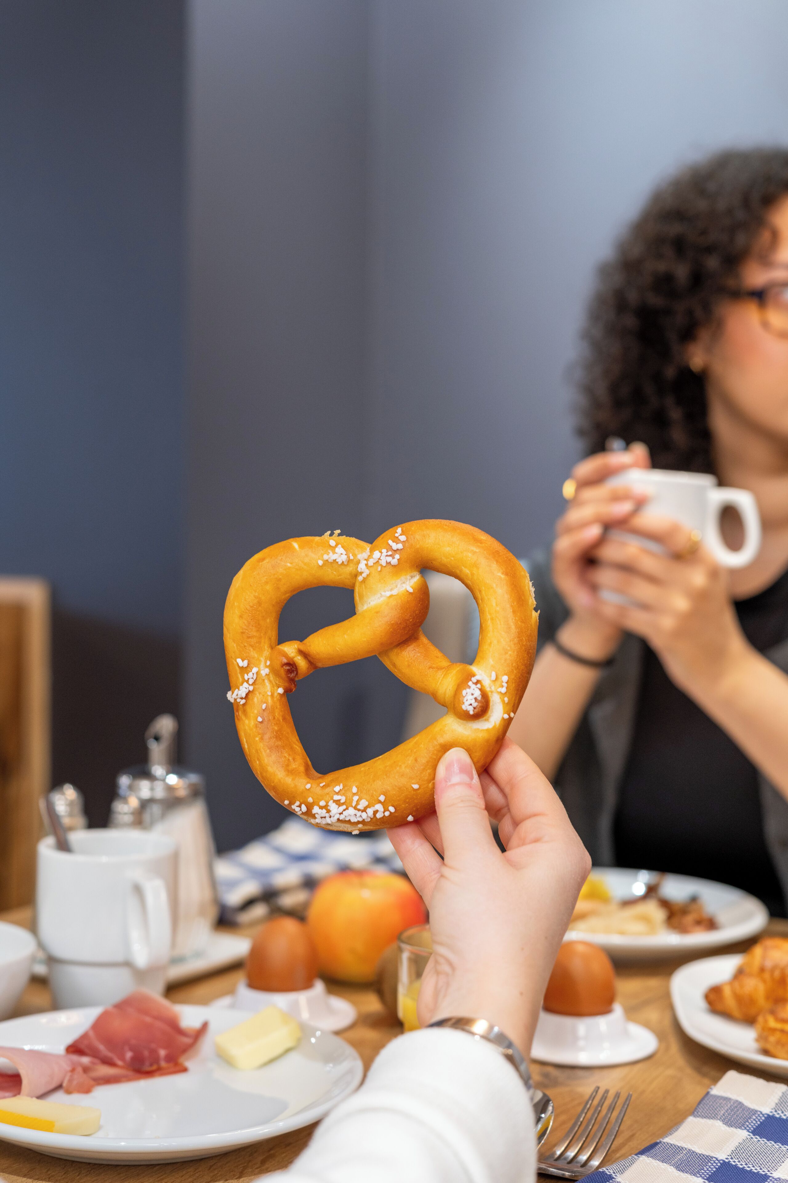 Une table à manger avec des assiettes remplies de nourriture, un bretzel et une tasse.