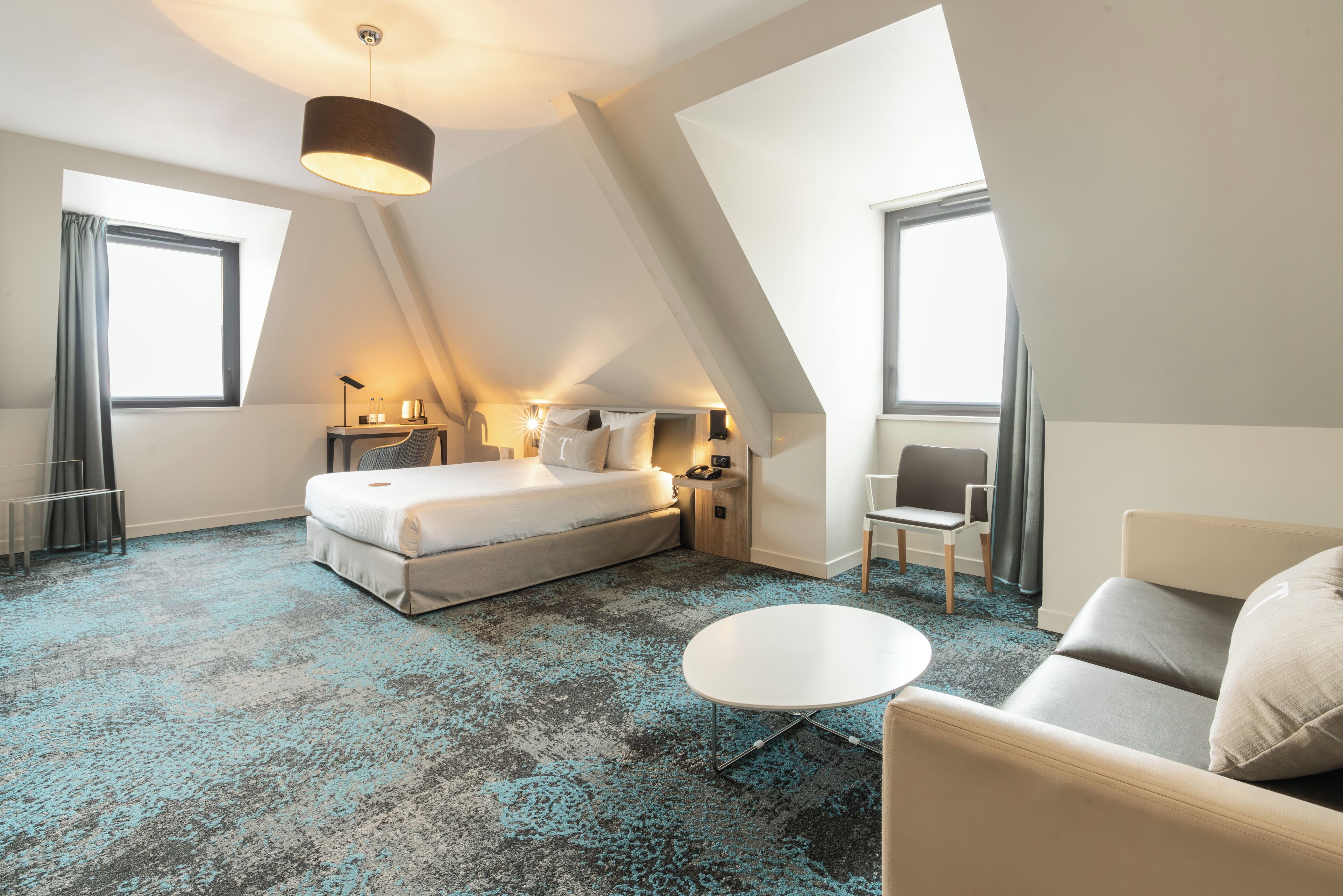 Une chambre d’hôtel moderne équipée d’un lit, d’une table ronde, d’un canapé et d’un bureau avec une chaise.