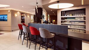 A modern bar area with a counter, bar stools, and shelves of glassware. - Hôtel Maison Turenne (Colmar)