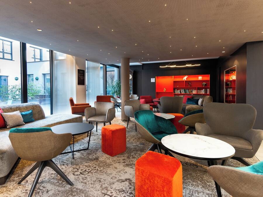 Un espace de détente moderne, doté de canapés, de fauteuils et d’une table basse, avec une grande fenêtre et une bibliothèque remplie de livres.